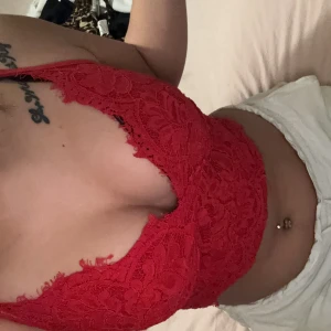 Röd spetslinne - Säljer en snygg röd spetslinne med vacker spetsdetalj. Toppen är ärmlös och har en croppad design som ger en trendig look. Perfekt för att lägga till en färgklick i garderoben. Storlek M men passar storlek s också 