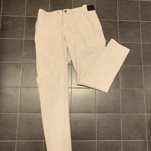 Beige kostymbyxor från Zara - Snygga beige kostymbyxor från Zara i herrstorlek M. Byxorna har en stilren design med knappar och dragkedja framtill. 