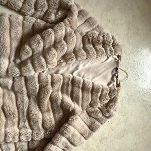 Beige pälsjacka från Gina Tricot - Säljer en supermjuk och fluffig beige pälsjacka från Gina Tricot. Jackan har en lyxig känsla med sitt täta pälsmaterial och är perfekt för kyligare dagar. Den har en stilren design utan krage och är helfodrad för extra komfort.