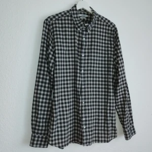 Rutig skjorta från J.Lindeberg - Snygg rutig skjorta från J.Lindeberg i svart och vit. Skjortan har en slim passform och långa ärmar med knappar framtill. Perfekt för en stilren look.