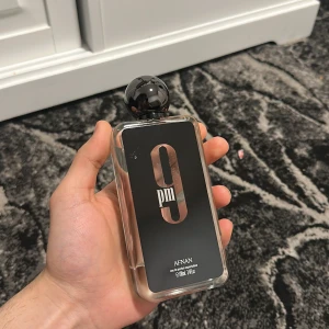 9 PM Eau de Parfum från Afnan - Säljer en elegant flaska av 9 PM Eau de Parfum från Afnan. Flaskan har en stilren design med svart etikett och en rund svart kork. Perfekt för kvällsanvändning med en sofistikerad doftprofil.