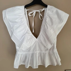 Volangtopp - Säljer denna populära vita blus/topp med volangdetaljer och knytning i ryggen. Storlek S! Ny!
