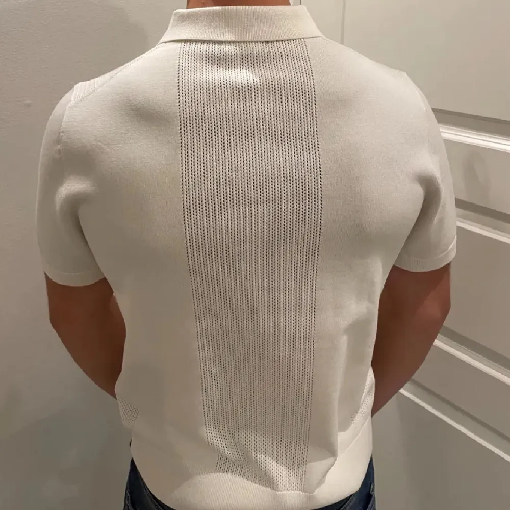 Snygg vit pikétröja från J.Lindberg med korta ärmar och texturerad panel fram och bak. Perfekt för en stilren och avslappnad look.. Neuleet.