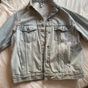 Ljusblå jeansjacka från Topshop - Säljer en snygg ljusblå jeansjacka från Topshop. Jackan har en klassisk design med knappar framtill och två bröstfickor med lock. Perfekt för en avslappnad stil.