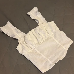 Vit topp från Gina Tricot - Säljer en söt vit topp från Gina Tricot med volangdetaljer på axelbanden. Den är tillverkad i ett lätt och luftigt material. Finns inte längre på Gina! 