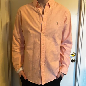 Rosa skjorta från Ralph Lauren - Säljer en stilren rosa skjorta från Ralph Lauren i slim fit. Skjortan har långa ärmar och är dekorerad med det klassiska broderade logotypen på bröstet. Perfekt för en elegant look.