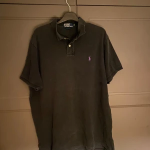 Svart kortärmad t-shirt från Polo Ralph Lauren - Säljer en stilren svart t-shirt från Polo Ralph Lauren. Den har korta ärmar och en klassisk krage med två knappar. Perfekt för en avslappnad och snygg look.