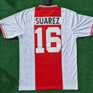 Vit och röd fotbollströja med Suarez 16 - Snygg fotbollströja i vitt och rött med Suarez och nummer 16 på ryggen. Tröjan har korta ärmar och ränder på ärmsluten. Perfekt för fotbollsfans!