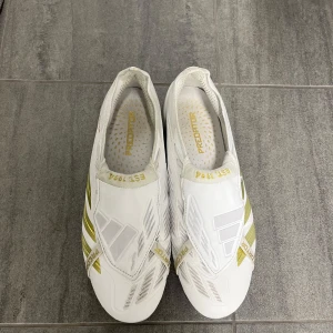 Vita Adidas Predator fotbollsskor - Säljer ett par vita Adidas Predator elite fotbollsskor med guldiga detaljer. Skorna är använda på 2 träningar och inget mer så de är i topp skick och är perfekta för fotbollsplanen. Original pris 2200kr