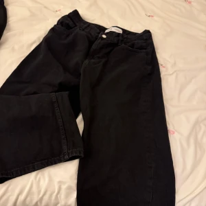 Svarta jeans från Bershka - Snygga svarta jeans från Bershka med klassisk femficksdesign. De har en knapp och dragkedja framtill och är perfekta för en stilren look. Passar bra till både vardag och mer uppklädda tillfällen.