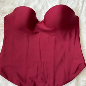 Vinröd korsett från H&M - Snygg trendig vinröd korsett från H&M i en elegant design. Den är axelbandslös och har en tight passform som framhäver figuren. Perfekt för att ge en stilren look. Har inte burit den, köpte förra månaden och har inte hunnit ha på mig den. Helt ny!