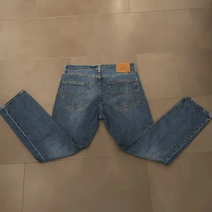 Blå jeans från Levi's ett par 502 - Klassiska blå jeans från Levi's med fem fickor och knappgylf. De har en straight passform och är perfekta för en avslappnad stil. Levi's logga syns på bakfickan.