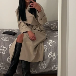 Beige trenchcoat - Snygg beige trenchcoat med knappar och bälte i midjan. Perfekt för höst och vår. Långärmad design med klassisk krage och stilren look.