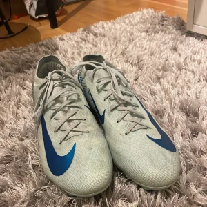 Nike Mercurial fotbollsskor  - Snygga vita Nike Mercurial fotbollsskor med blå detaljer och snörning. Perfekta för fotbollsplanen med sin lätta och smidiga design. Nypris 1999