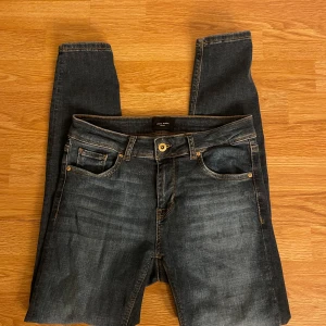 Mörkblå jeans från Vero Moda - Snygga mörkblå jeans från Vero Moda med klassisk femficksdesign och guldfärgade knappar. Jeansen har en rak passform och är perfekta för en avslappnad stil. Tillverkade i slitstarkt denimtyg.