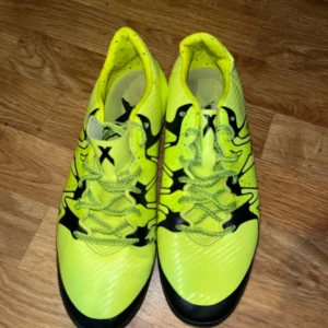 Gula fotbollsskor från Adidas - Säljer ett par gula fotbollsskor från Adidas med svarta detaljer och snörning. Skorna har en iögonfallande design och är perfekta för fotbollsplanen. De är märkta med Adidas logotyp på hälen.