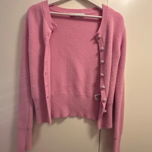 Rosa kofta med pärlknappar - Söt rosa kofta med långa ärmar och dekorativa pärlknappar. Perfekt för att lägga till en touch av elegans till din outfit. Mjuk och bekväm att bära.