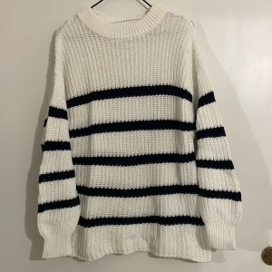 Vit och blå randig stickad tröja - Säljer en mysig vit stickad tröja med blåa ränder. Tröjan har en avslappnad passform och långa ärmar, perfekt för kyligare dagar. Den ribbade halsringningen och muddar ger en klassisk look. Perfekt för höst och vinter!