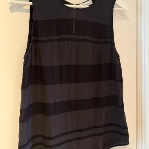 Svart ärmlös topp från Samsøe & Samsøe - Snygg svart ärmlös topp från Samsøe & Samsøe med breda horisontella ränder. Perfekt för en stilren look. Tillverkad i ett mjukt material som ger en bekväm passform. Jag är osäker på storleken men skulle säga att den passar både S och M. Jag brukar kunna ha både S och M i toppar. Den här sitter något tight över brösten men ändå okej ☺️