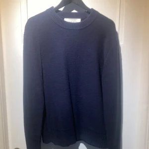 Mörkblå ulltröja från A Day's March - Säljer en stilren mörkblå tröja från A Day's March i 100% ull. Tröjan har en klassisk design med rund hals och långa ärmar.