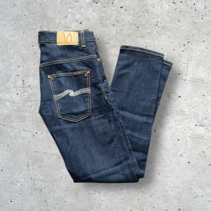Mörkblå jeans från Nudie Jeans - Snygga mörkblå jeans från Nudie Jeans med klassisk femficksdesign och kontrastsömmar. Jeansen har en rak passform och är tillverkade i högkvalitativt denim. Perfekta för en stilren look.