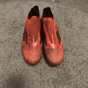 Röda fotbollsskor från Adidas - Säljer ett par röda Adidas fotbollsskor med svarta detaljer. Skorna har en strömlinjeformad design och är perfekta för snabba rörelser på planen. De har en klassisk dobbsula för bra grepp.