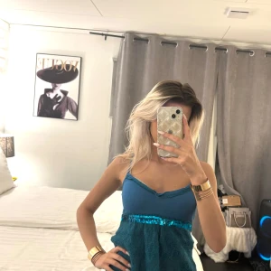 Blå topp med paljettdetaljer - Snygg blå topp med glittriga paljettdetaljer i midjan. Toppen har smala axelband och en åtsittande passform upptill. Perfekt för en kväll ute eller en speciell tillställning.