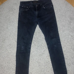 Mörkblå jeans från Nudie Jeans w31L32 - Snygga mörkblå jeans från Nudie Jeans med en slim passform. De har klassisk femficksdesign och knappar i midjan. Perfekta för en stilren look.
