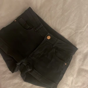 Svarta shorts med fickor - Snygga svarta shorts med klassisk design och praktiska fickor både fram och bak. De har en knapp och dragkedja framtill för enkel stängning. Perfekta för en stilren look.