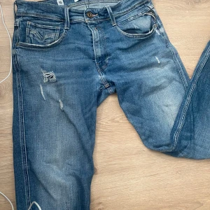 Replay jeans - Snygga blå jeansbyxor från Replay, modell Anbass. De har en slim fit passform och är dekorerade med slitningar för en trendig look. Klassisk femficksdesign med knapp och dragkedja i gylfen. Priset är inte hugget i sten och kan även ta emot byten!