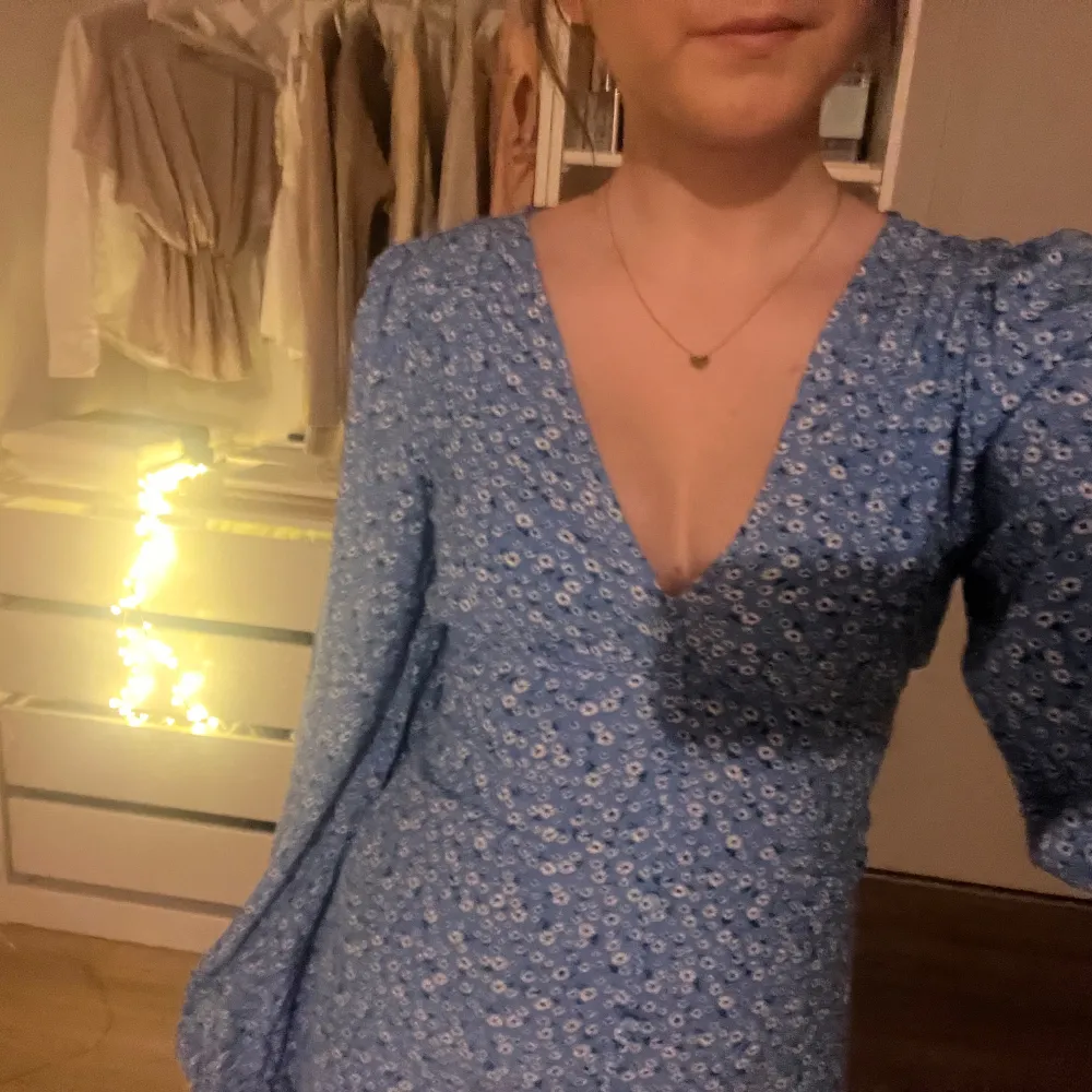 Säljer en söt blå klänning med blommigt mönster. Klänningen har en v-ringad design och långa ärmar, perfekt för vår och sommar. Den är i en normal passform och har en elegant längd. Köpt för 800kr om jag minns rätt, säljer för 300💗. Mekot.