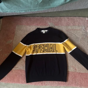 tröja från H&M - Säljer en svart tröja från H&M med en gul rand och texten 'SPECIAL' över bröstet. Tröjan har långa ärmar och en rund halsringning. Perfekt för en avslappnad stil.