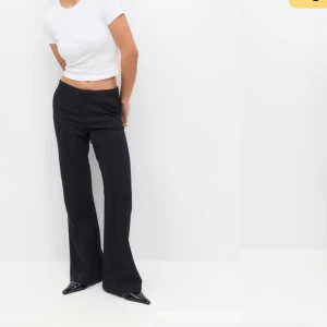 Svarta kostymbyxor - Snygga svarta kostymbyxor med bootcut-stil. De är högmidjade och har en elegant passform som passar perfekt för en stilren look. Byxorna är tillverkade i ett mjukt och bekvämt material.