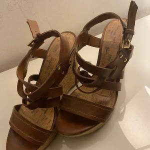 Bruna kilklackssandaler - Snygga bruna sandaler med kilklack och flera remmar. Sandalerna har en justerbar rem runt ankeln och en flätad sula som ger en somrig känsla. 