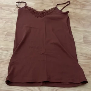 Brun linne med spetsdetaljer - Säljer ett brunt linne med smala axelband och vacker spetsdetalj vid halsringningen. Perfekt för lager-på-lager eller som det är. Superbekvämt och stilrent!