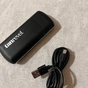 Tanrevel  med USB-kabel - Säljer en svart Tanrevel enhet som kommer med en USB-kabel för laddning. Perfekt för att uppnå en jämn och solkysst look hemma. Enheten är kompakt och lätt att ta med sig, vilket gör den idealisk för resor.