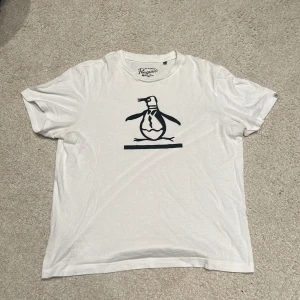 Vit t-shirt från Original Penguin - Säljer en vit t-shirt från Original Penguin med ett coolt pingvintryck på framsidan. T-shirten är kortärmad och har en klassisk rund halsringning. Perfekt för en avslappnad stil. 🐧storlek S