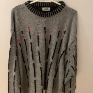 Grå och svart tröja från Moschino - Snygg grå tröja från Moschino med svarta vertikala ränder och röd textdetalj. Tröjan har en ribbad krage och långa ärmar, perfekt för en stilren look. Passar bra till både jeans, den är knappt använd och fungerar till det mesta. Det är XL men fungerar som L. Pris går att diskuteras.