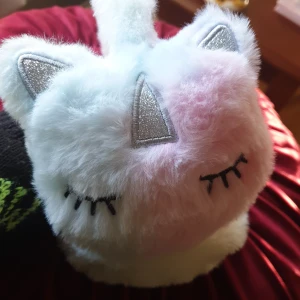 Öronmuffar  - Oanvänd. Söt och fluffiga öronmuffar med katt/unicorn motiv i vitt, rosa, blått o grönt. Diademet har glittriga öron och stängda ögon som detaljer. Perfekt för att hålla värmen och se gullig ut samtidigt!