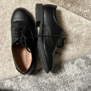 Svarta skor från School Ride - Snygga svarta skor från School Ride med snörning och robust sula. Perfekta för en stilren look. Skorna har en klassisk design med rund tå och är tillverkade i syntetmaterial.