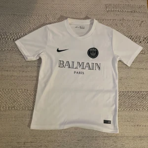 Vit fotbollströja från Nike x Balmain - Snygg vit fotbollströja från Nike i samarbete med Balmain! Tröjan har en stilren design med Balmain Paris-logga och Nike-märke på framsidan 🇫🇷Perfekt för fotbollsfans som vill ha något unikt och trendigt 🔥Tröjan är S men passar även M. Skriv direkt vid vidare frågor 😁