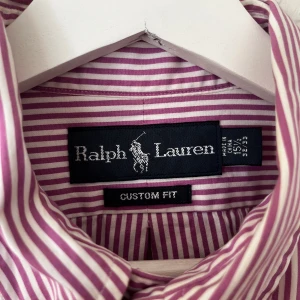 Rosa randig skjorta från Ralph Lauren - Snygg randig skjorta från Ralph Lauren i lila och vit med broderad logga på bröstet. Sitter som storlek M-L. Väldigt bra skick!