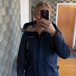 Mörkblå jacka från Didriksons - Säljer en mörkblå jacka från Didriksons med luva och dragkedja. Jackan har långa ärmar och flera praktiska fickor med knappar. Perfekt för vår väder och har en stilren design. Använd men i gott skick