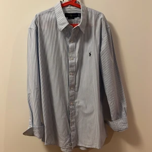 Randig skjorta från Ralph Lauren - Snygg och klassisk blå- och vitrandig skjorta från Ralph Lauren. Skjortan har långa ärmar och en broderad logga på bröstet. Perfekt för en stilren look.