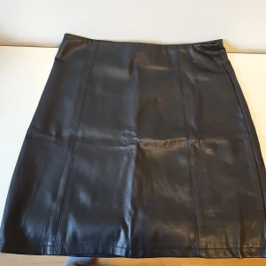 Svart kjol från Amisu - Snygg svart kjol från Amisu i skinnimitation med dragkedja bak. Perfekt för en stilren look. Tillverkad i polyuretan och polyester.