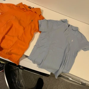 Två pikétröjor från Ralph Lauren - Säljer två snygga pikétröjor från Ralph Lauren. En i ljusblått och en i orange, båda med klassisk krage och knappdetaljer. Perfekta för en stilren look. I storlek S och dom är hel nya aldrig använda och vill ha 200kr st för dom