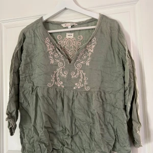 Grön blus med broderi från Odd Molly - Säljer en vacker grön blus från Odd Molly med detaljerat broderi i vitt på både fram- och baksidan. Blusen har långa ärmar med spets detaljer  och en v-ringad hals med spetskant. Perfekt för en bohemisk stil. Jättefin blus som är sparsamt använd, fint skick! Väldigt skrynklig på bilden men går lätt att ordna vid strykning! Vid frågor och funderingar hör av er, jag svarar så fort jag kan!🩷