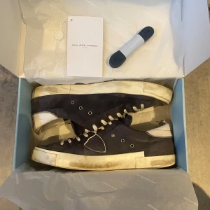 Svarta sneakers från Philippe Model - Snygga blå sneakers från Philippe Model med vita detaljer och snörning. Skorna har en klassisk design med en robust sula och är perfekta för en avslappnad stil. Inkluderar extra skosnören och box. Skorna är ganska slitna som man ser på bilderna