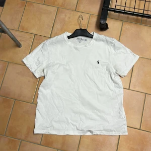 Vit t-shirt från Ralph Lauren - Säljer en klassisk vit t-shirt från Ralph Lauren med den ikoniska broderade loggan på bröstet. T-shirten är kortärmad och tillverkad i mjuk bomull. Perfekt för en avslappnad stil.