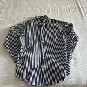 Randig skjorta från Ralph Lauren - Snygg och stilren randig skjorta från Ralph Lauren Sport i slim fit. I storlek S. Perfekt för en elegant look.